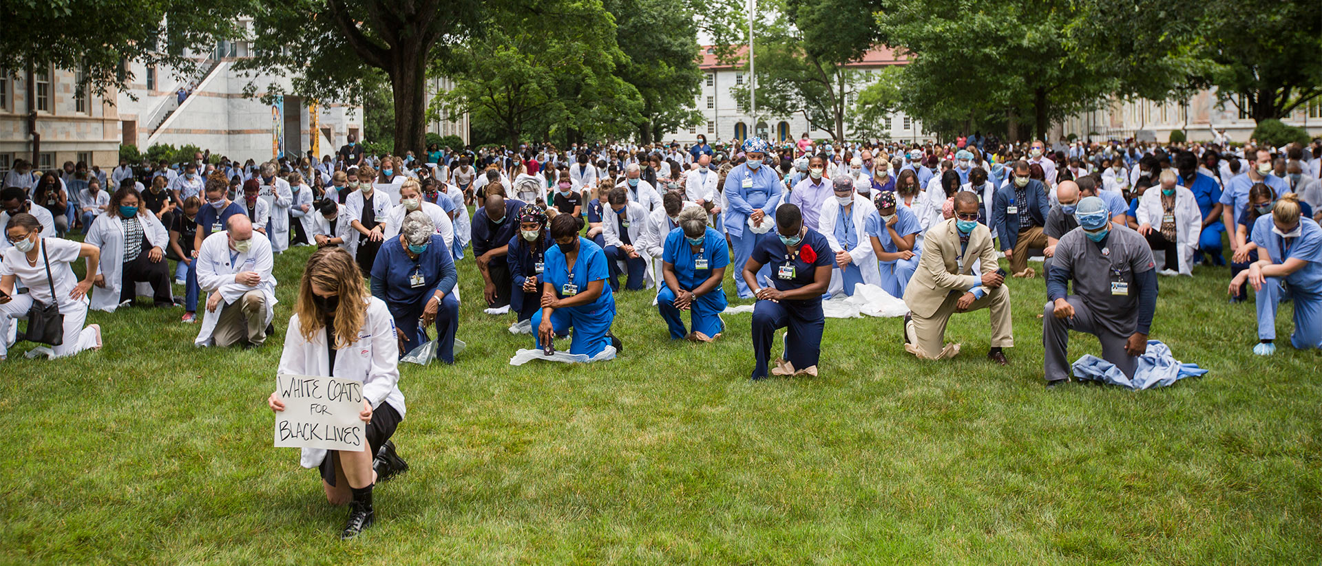 large group of medical students in white coats kneeling on the Emory quad