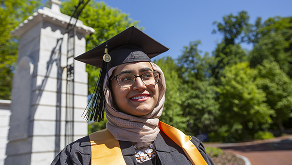 graduating student in cap and gown wearing head scarf and glasses