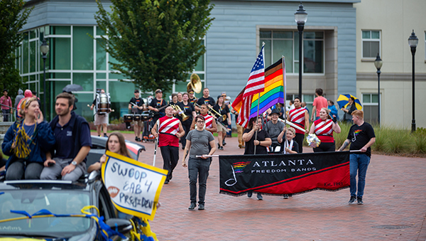Emory Homecoming featuring marchers with LGBT and American flags and banner reading American Freedom Bands